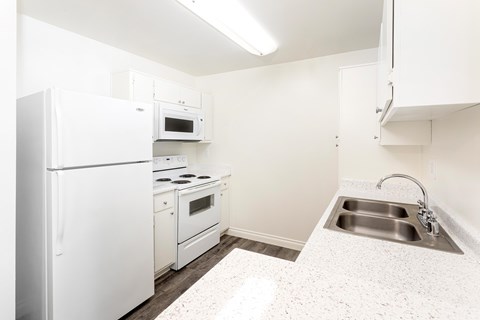 A white kitchen with a refrigerator, oven, and sink.