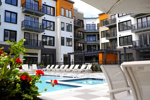 A pool surrounded by lounge chairs and flowers in front of apartment buildings.