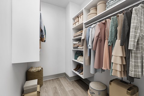 A white closet with clothes hanging and shelves with shoes and baskets.