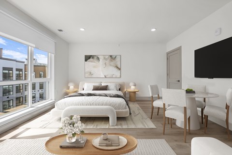 A modern studio bedroom with a large bed and a window.