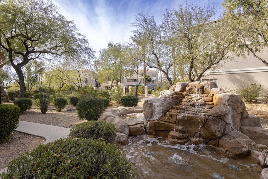 A small waterfall in a garden with rocks and shrubs.at Vintage at Scottsdale, Arizona