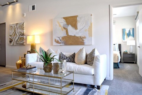 A living room with a white couch, a glass coffee table, and a large abstract painting on the wall.