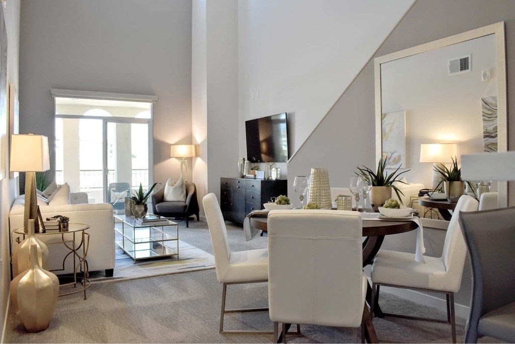 A modern living room with white furniture and a staircase in the background.
