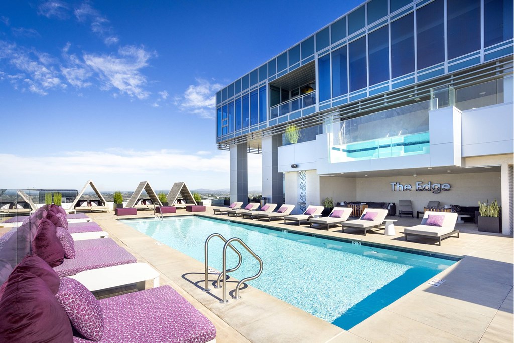A pool area with lounge chairs and a building in the background. at LUX by Garden*, San Diego, CA