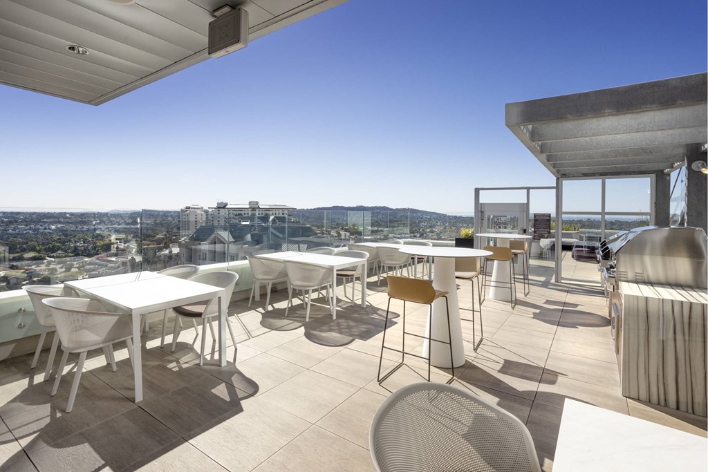 A patio with white chairs and tables overlooks a cityscape. at LUX by Garden*, San Diego