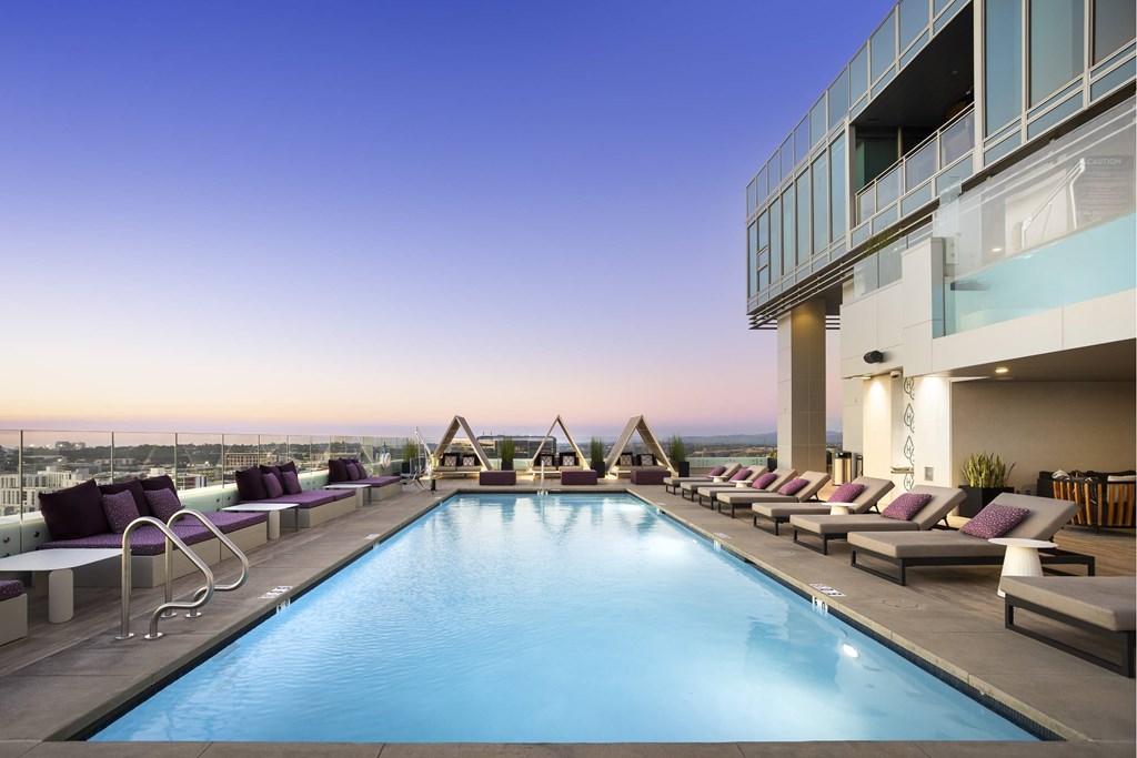 A large swimming pool with lounge chairs on a terrace overlooking a cityscape at dusk. at LUX by Garden*, San Diego