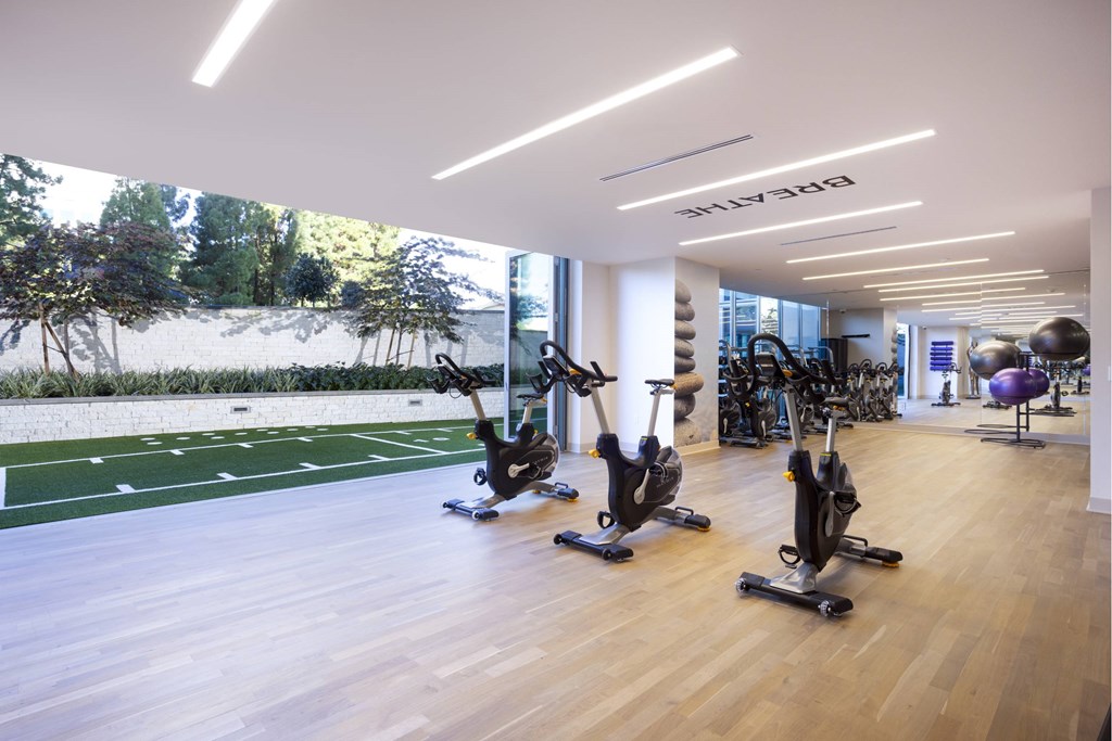A gym with exercise bikes and a large window showing a green landscape. at LUX by Garden*, San Diego, 92122