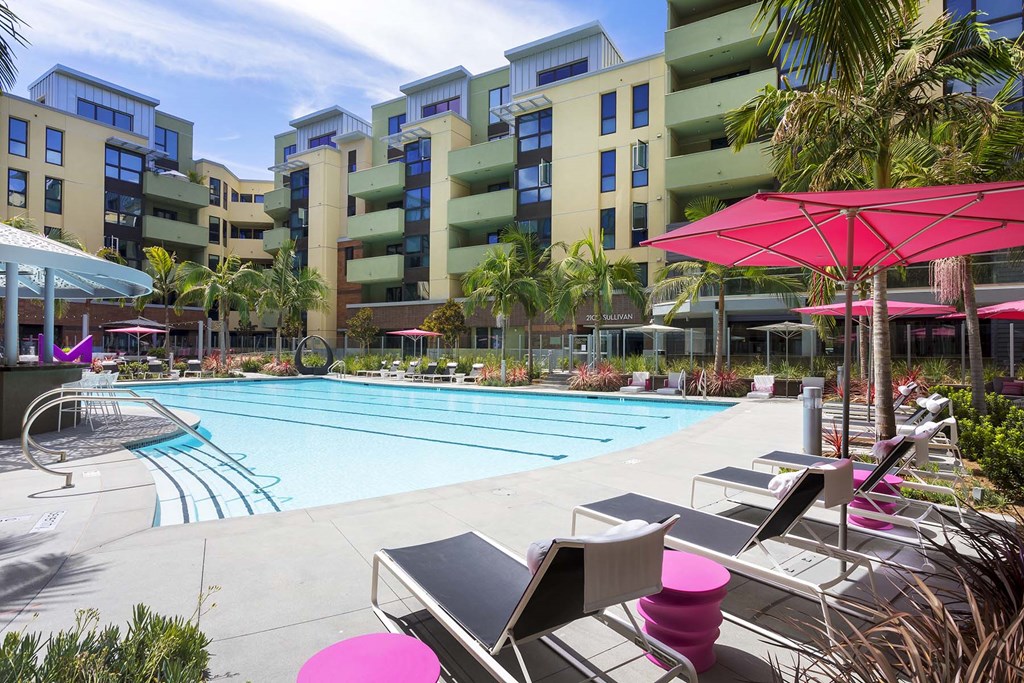 A pool area with a pink umbrella and chairs.
