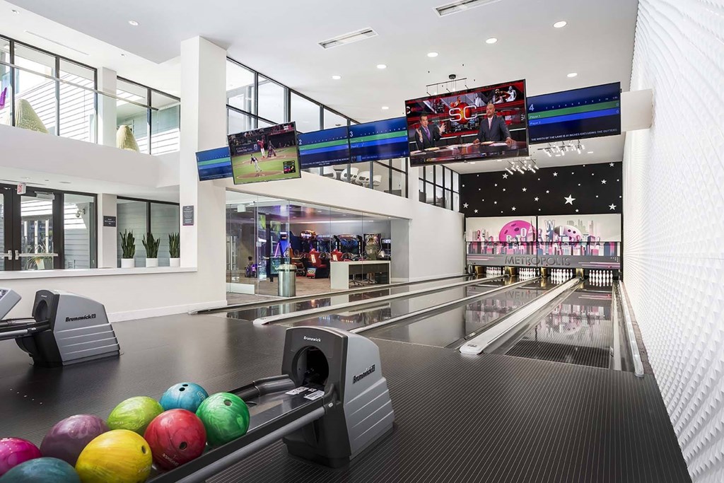 A bowling alley with a row of bowling balls in front of the lanes.