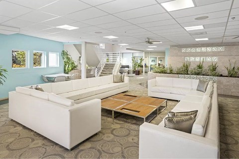 A spacious living room with white furniture and a staircase in the background.