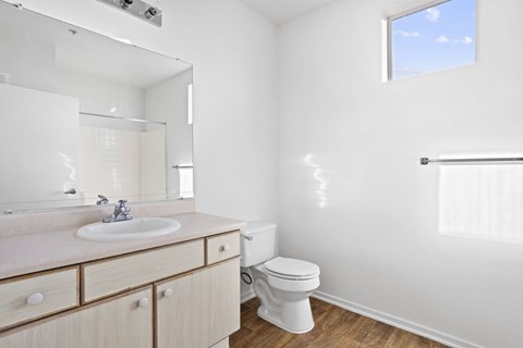 A white bathroom with a toilet, sink, and mirror.at Costa Verde Village Apartments, San Diego, CA 92122