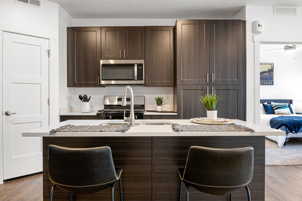 a kitchen with dark cabinets and a large island with a sink and two chairs