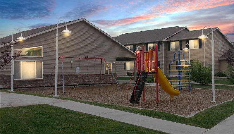 A playground with a slide and a climbing frame is situated in front of a building.