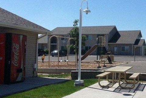 A playground with a slide and picnic tables is in front of a building.
