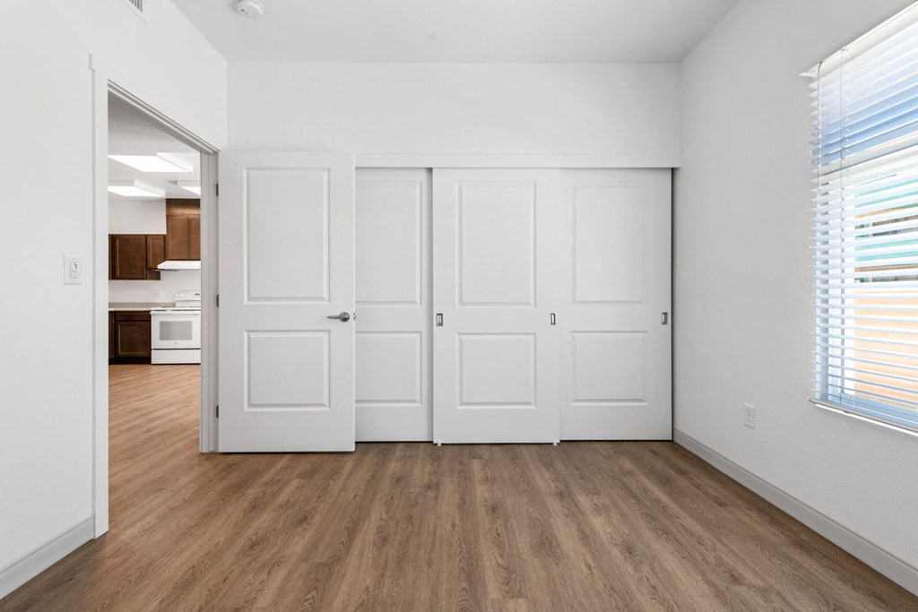 a bedroom with two doors and a kitchen in the background