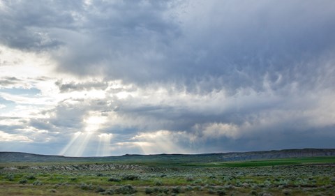 The sun is shining through the clouds over a green landscape.