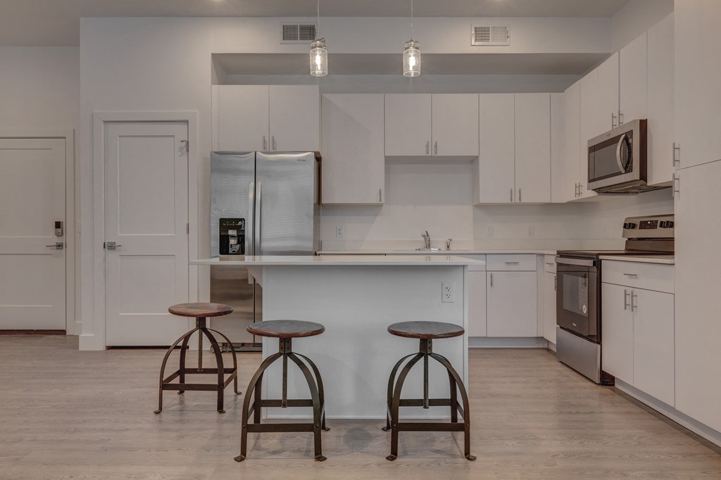 A kitchen with white cabinets and a white island with two stools in front.