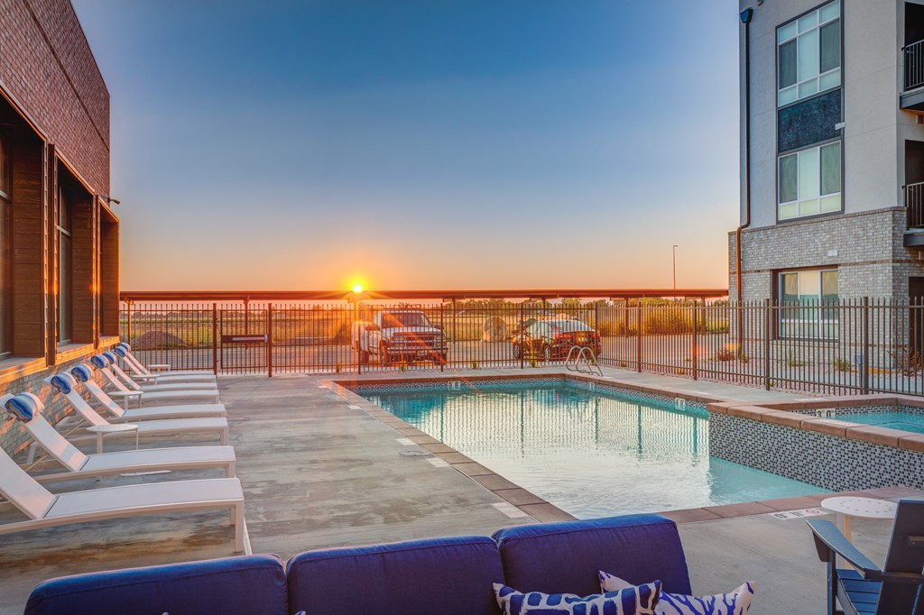 A sunset view from a rooftop pool area with lounge chairs and a fence.