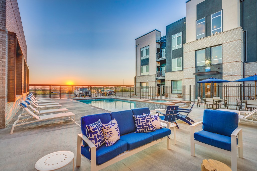 A sunset view of a pool area with a blue sofa and chairs.