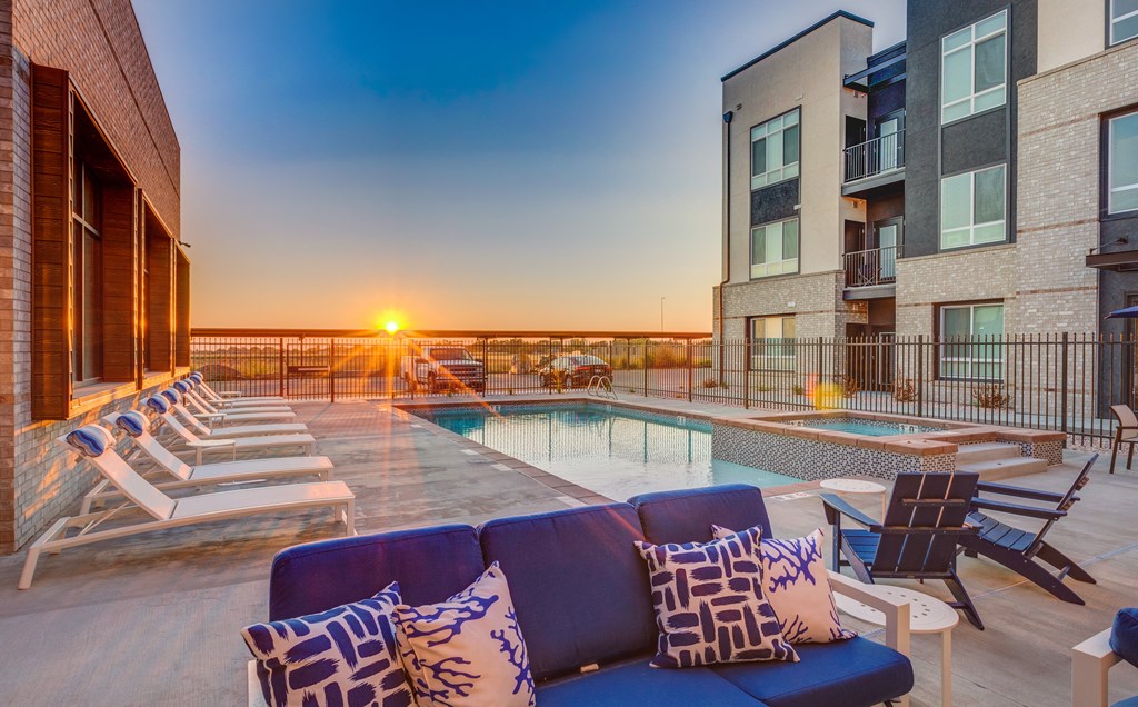 A sunset view from a rooftop pool area with lounge chairs and a couch.