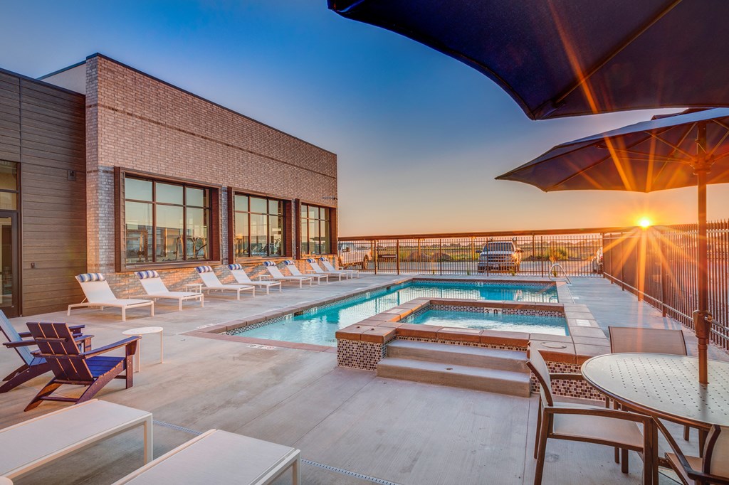 A sunset view of a pool area with lounge chairs and a building.