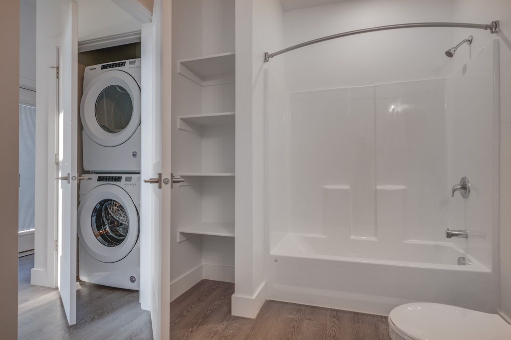 A white washing machine is in a small bathroom with a walk-in shower.