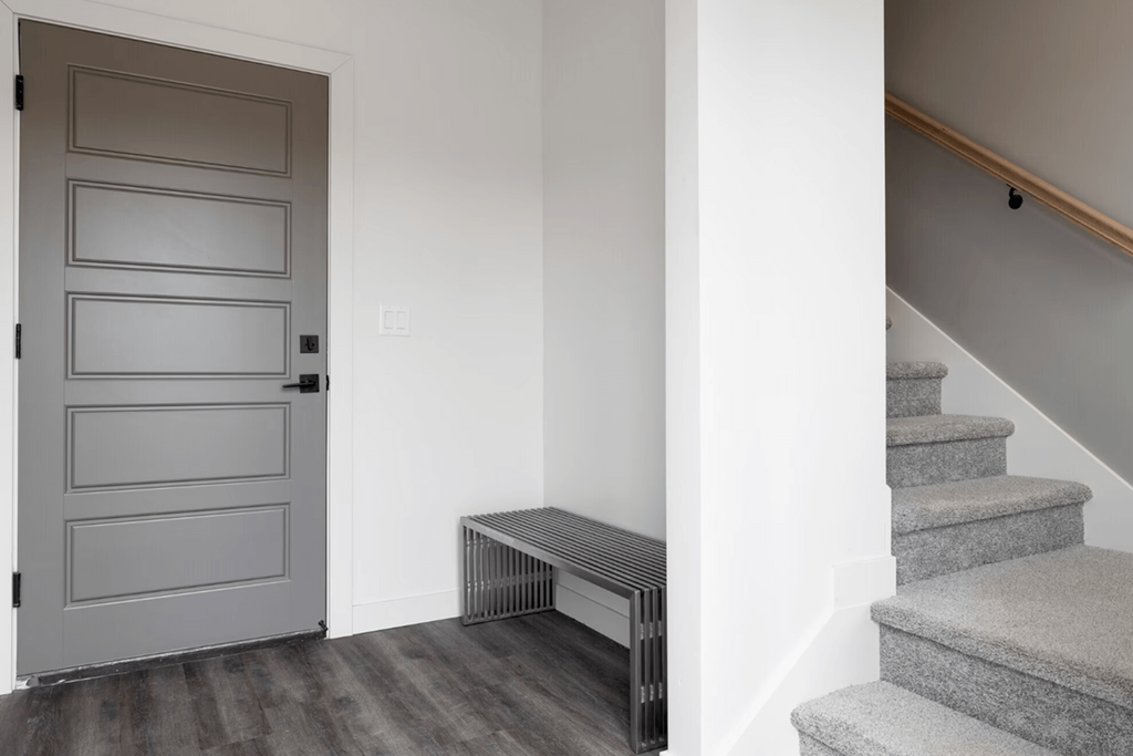 a gray door in a white room with stairs and a radiator