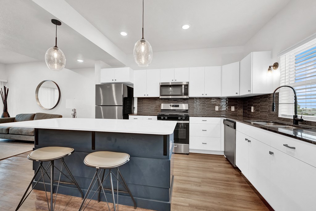 a kitchen with white cabinets and a bar with three stools