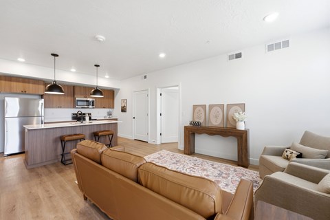 A modern living room with a brown sofa and a kitchen area in the background.