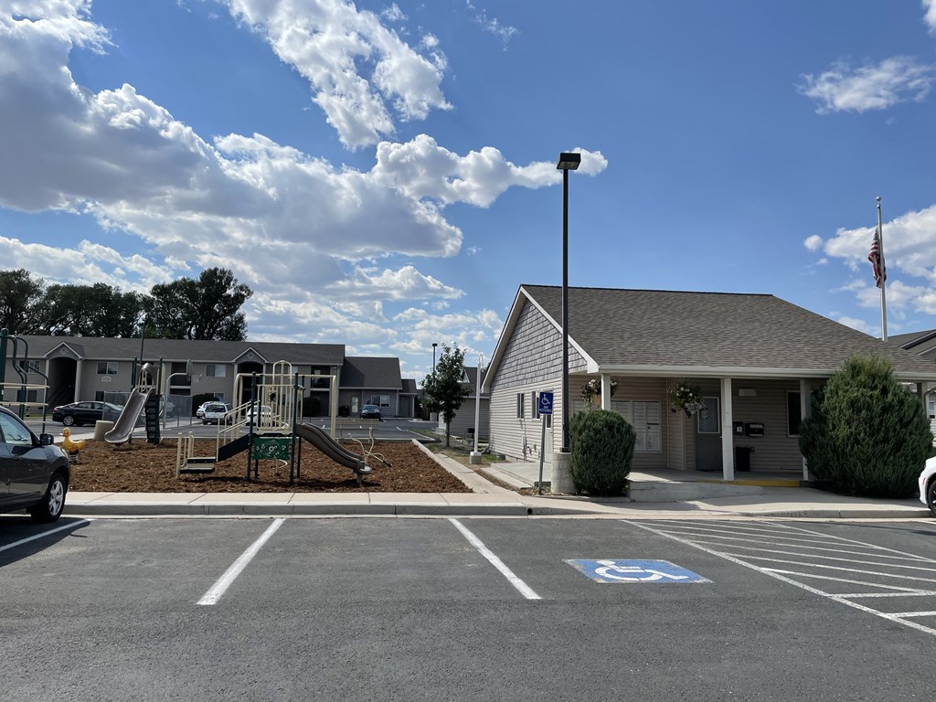 A parking lot with a playground and a building in the background.