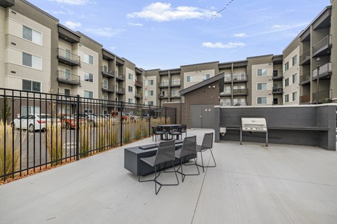 A patio with a table and chairs is surrounded by a black fence and apartment buildings.