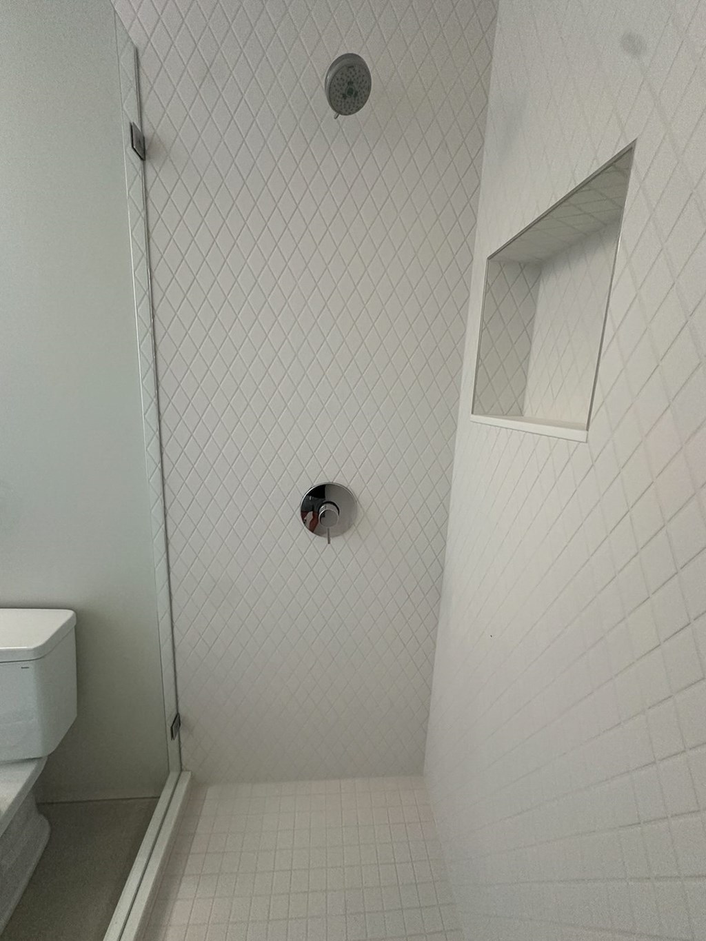 a white tiled bathroom with a shower and a toilet