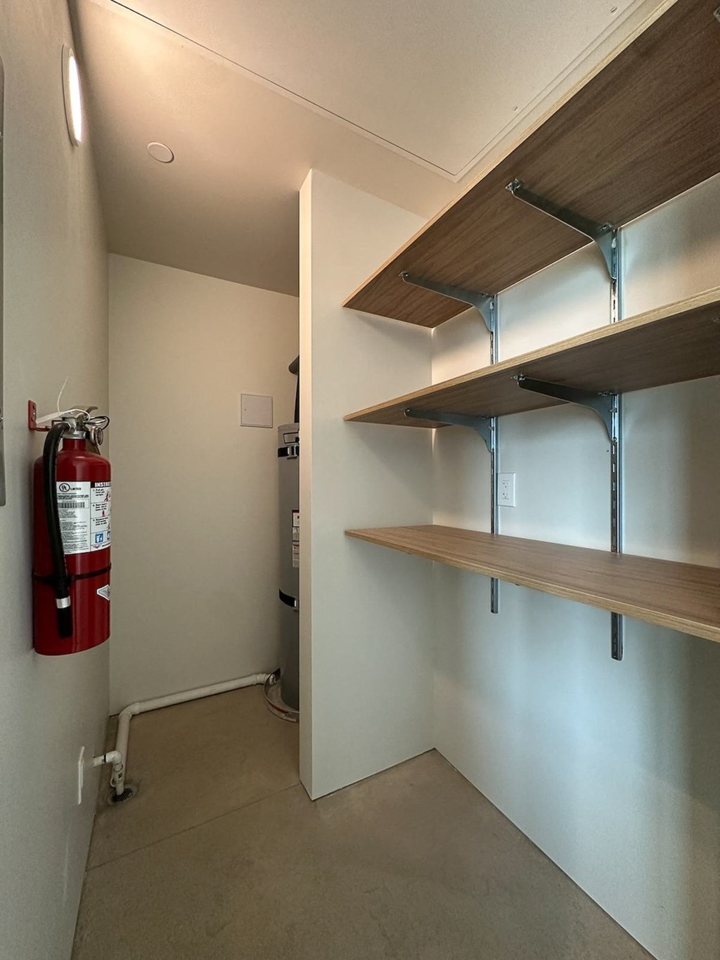 A room with a fire extinguisher on the wall and shelves on the wall.