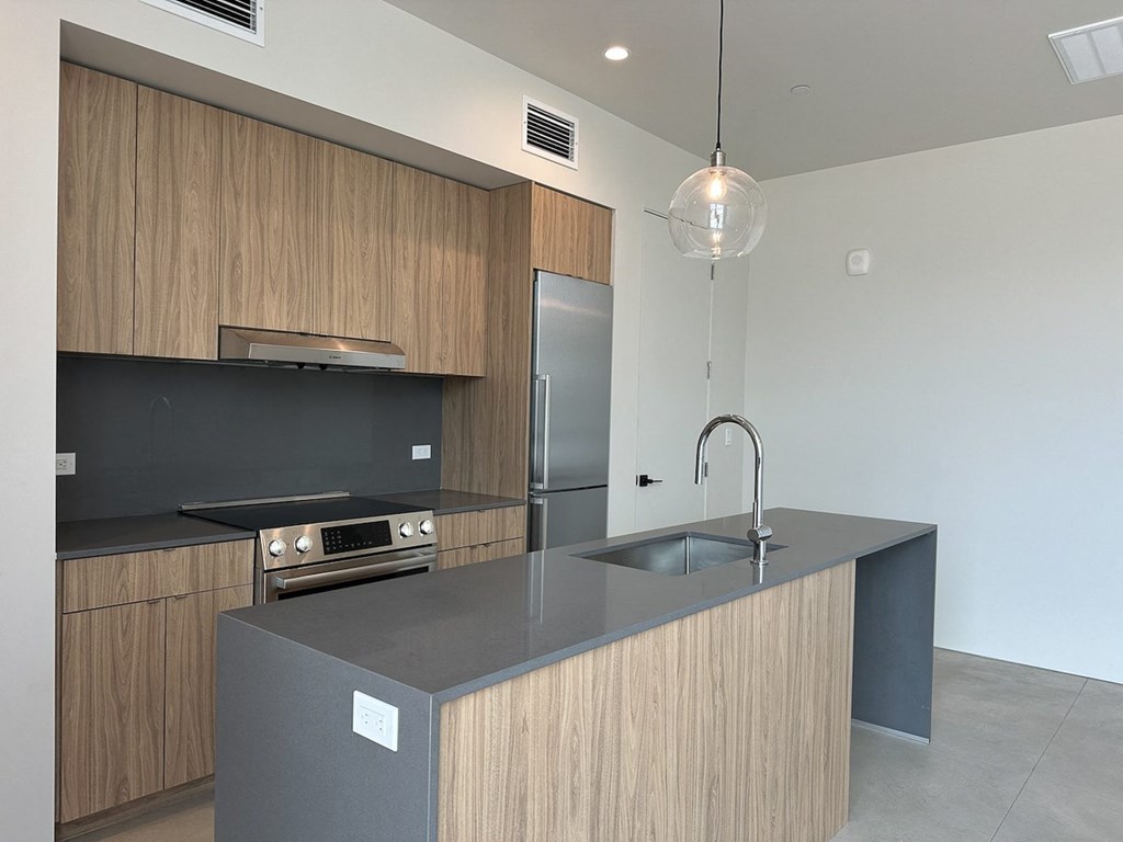 A modern kitchen with a dark countertop and wooden cabinets.