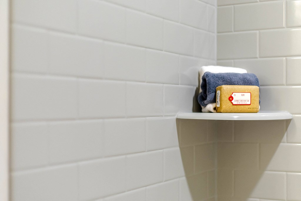 a bathroom with a white tiled wall and a shelf with towels and a box