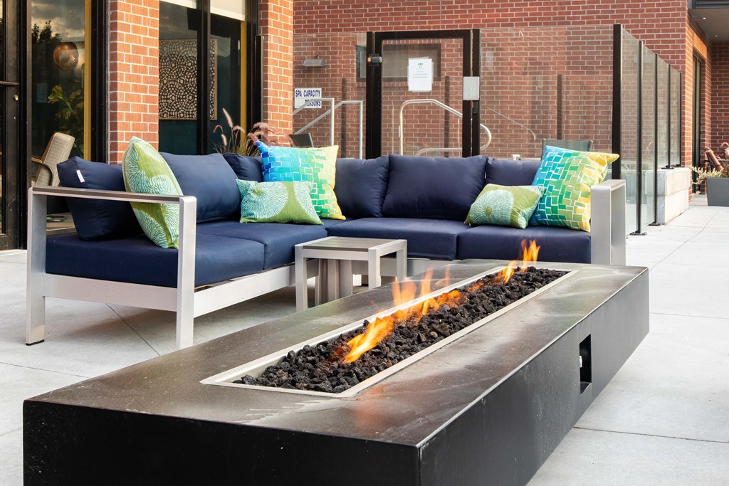 a patio with couches and a fire pit in front of a brick building