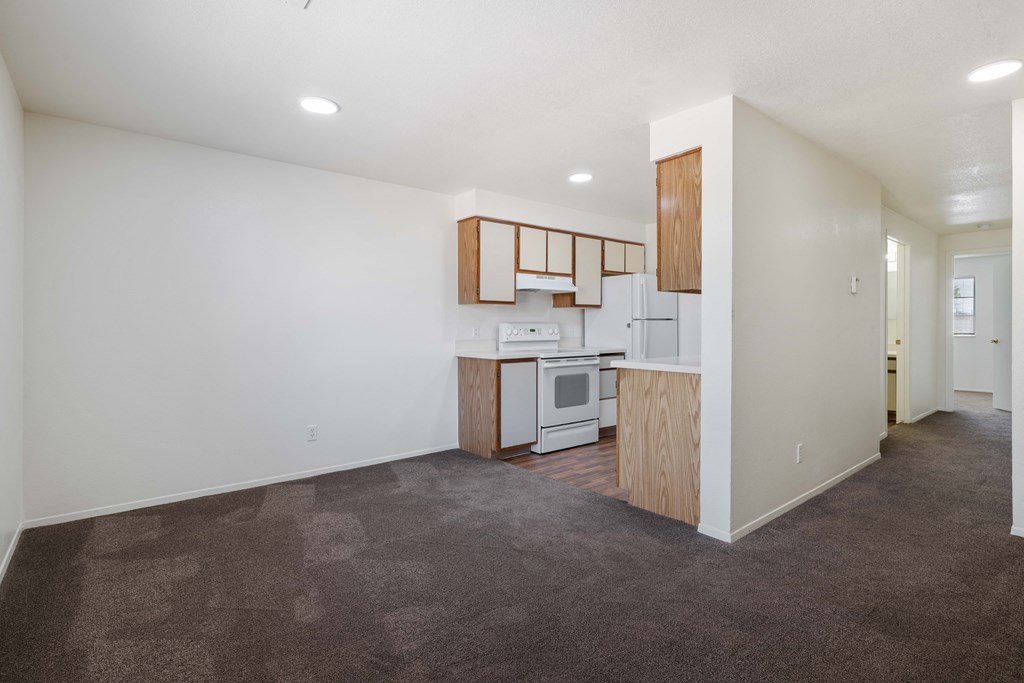 an empty living room and kitchen with white walls and brown carpet