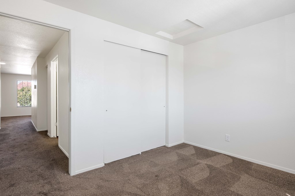 a living room with white walls and carpet and a door to a hallway