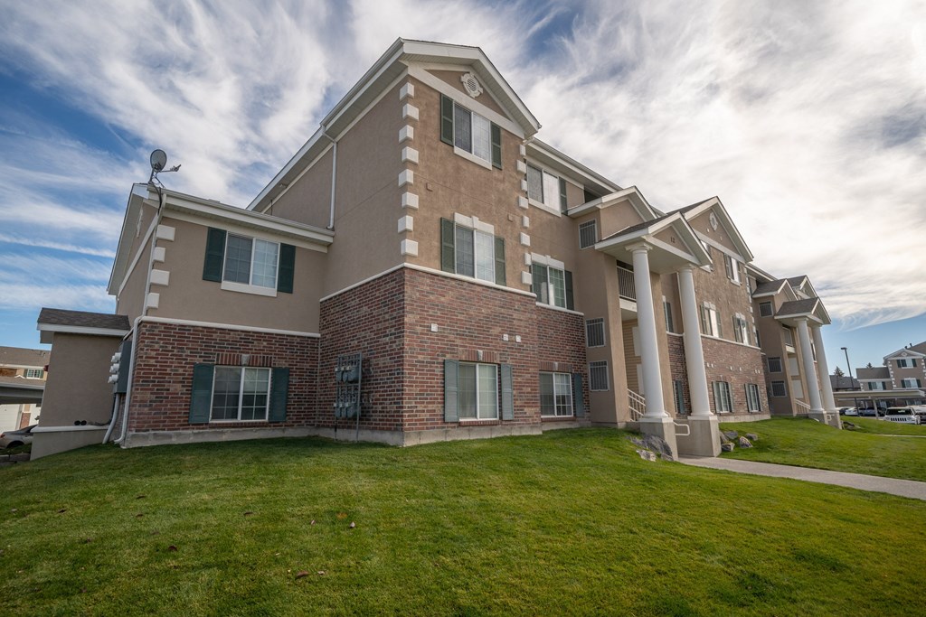 an apartment building with a green lawn and a cloudy sky
