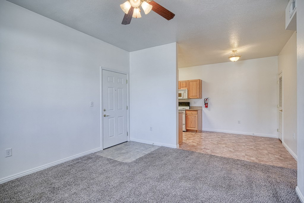 a living room with a ceiling fan and a kitchen in the background