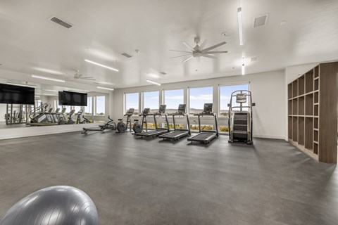 A spacious gym with treadmills, elliptical machines, and a fan.