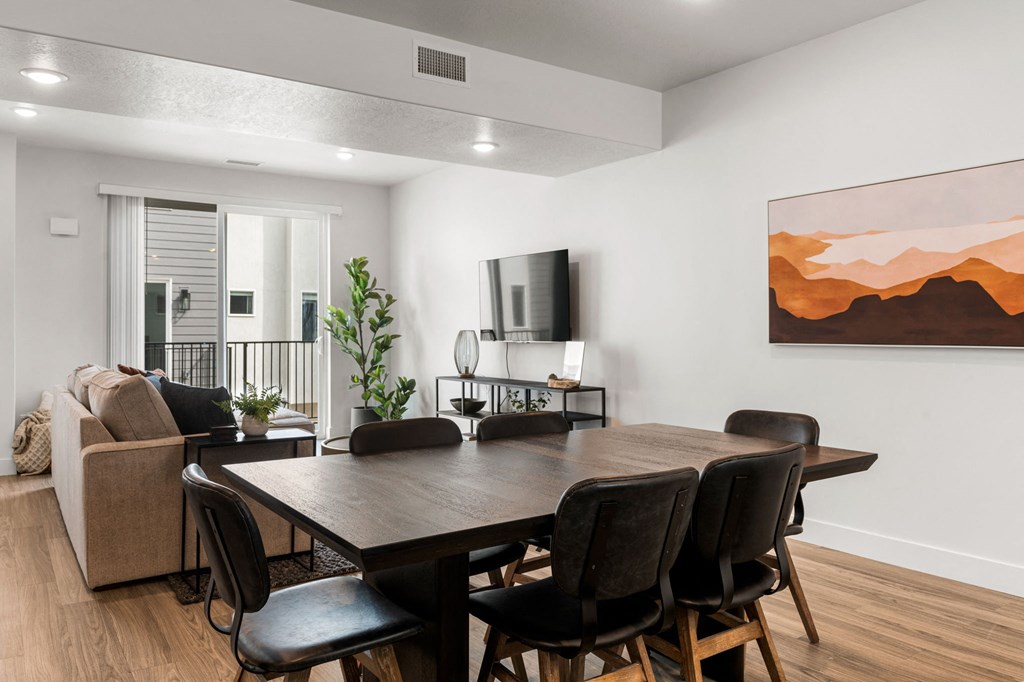 a dining room table with chairs and a couch in a room with white walls and hardwood