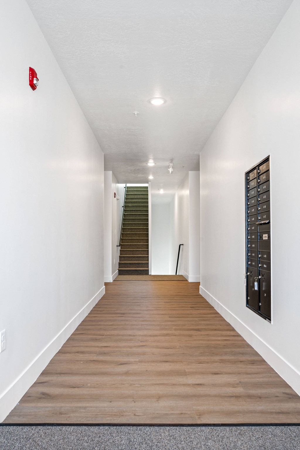 a long hallway with white walls and wood floors and a staircase
