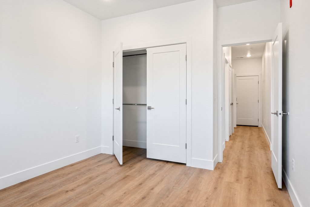 a bedroom with white walls and wood floors and a closet