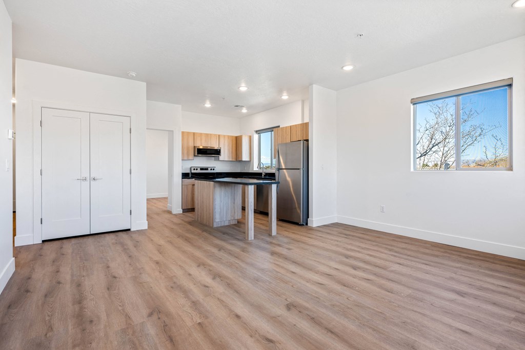 an empty living room with a kitchen with a large window