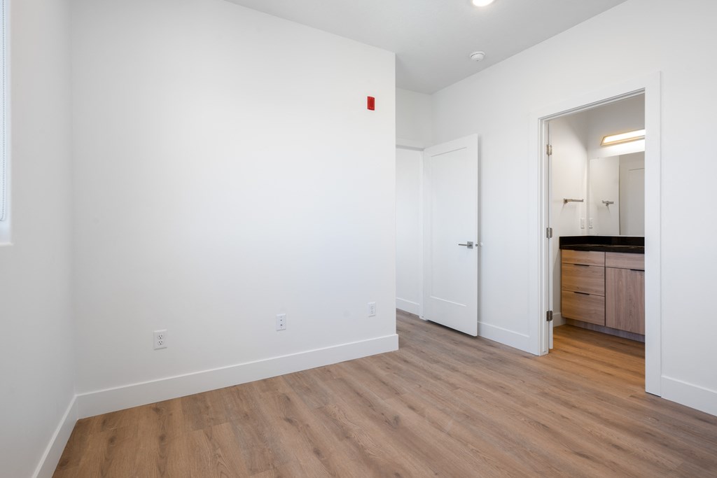 a bedroom with white walls and wood flooring and a door to a bathroom