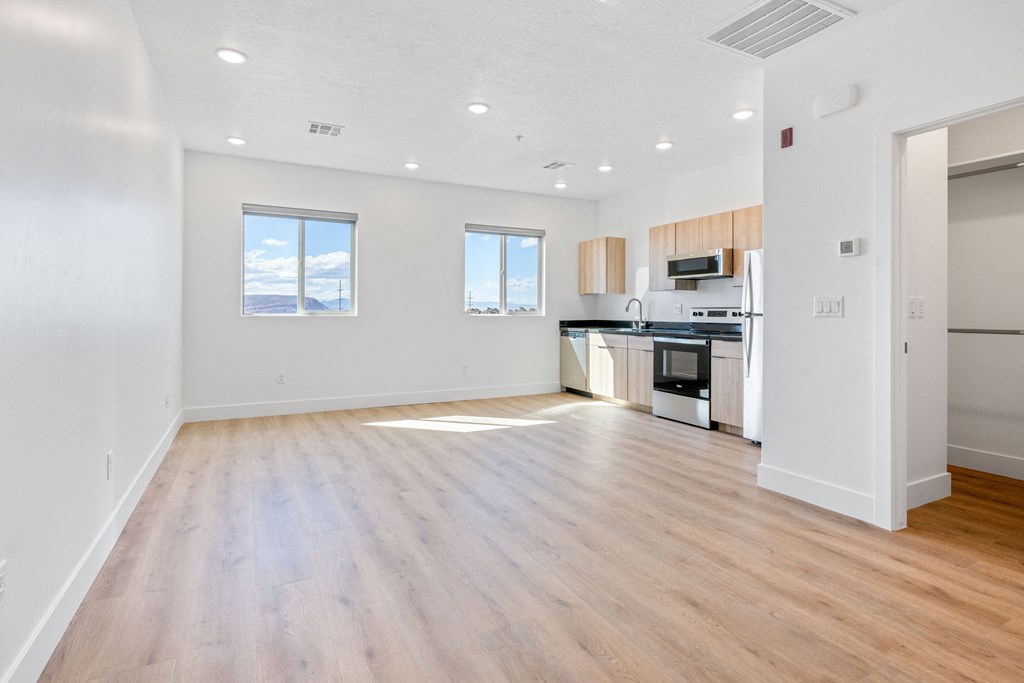 an empty living room and kitchen with wood floors and white walls