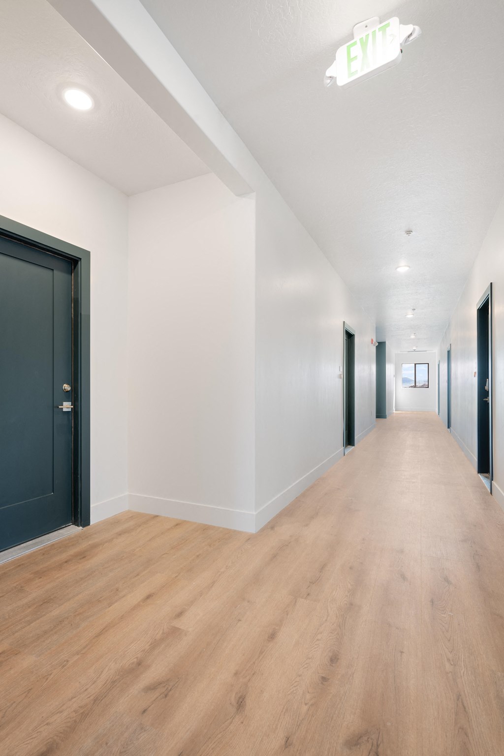 a corridor with white walls and wood floors and black doors