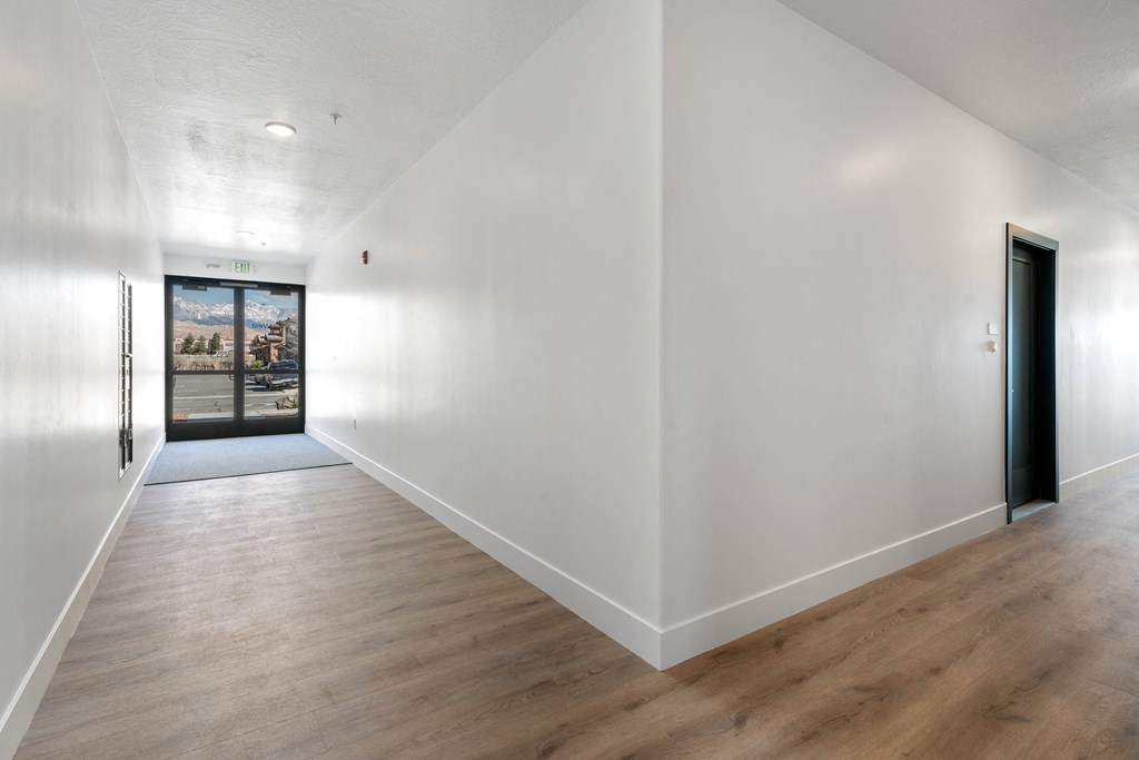 a hallway with white walls and wood floors and a black door