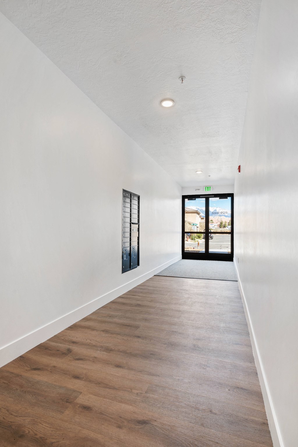 a hallway with white walls and wood floors and a glass door